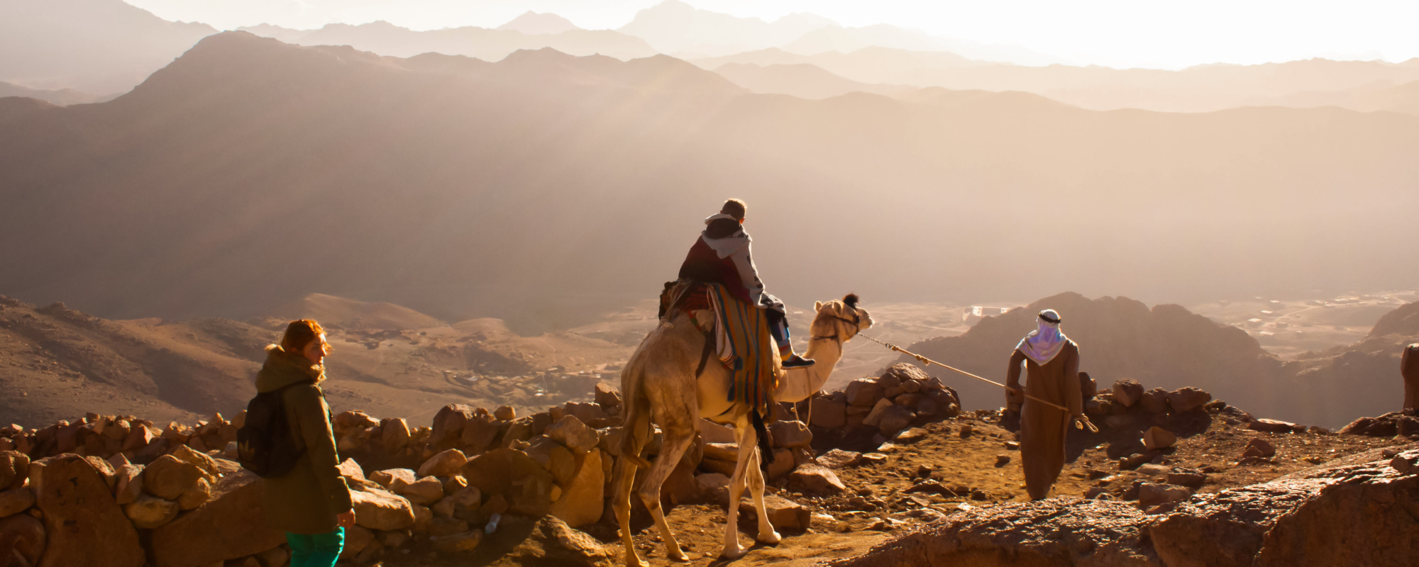 Ägypten - Kamel mit Reiter, Kamelführer, Frau laufend auf Mosesberg, im Hintergrund Berge und Tal