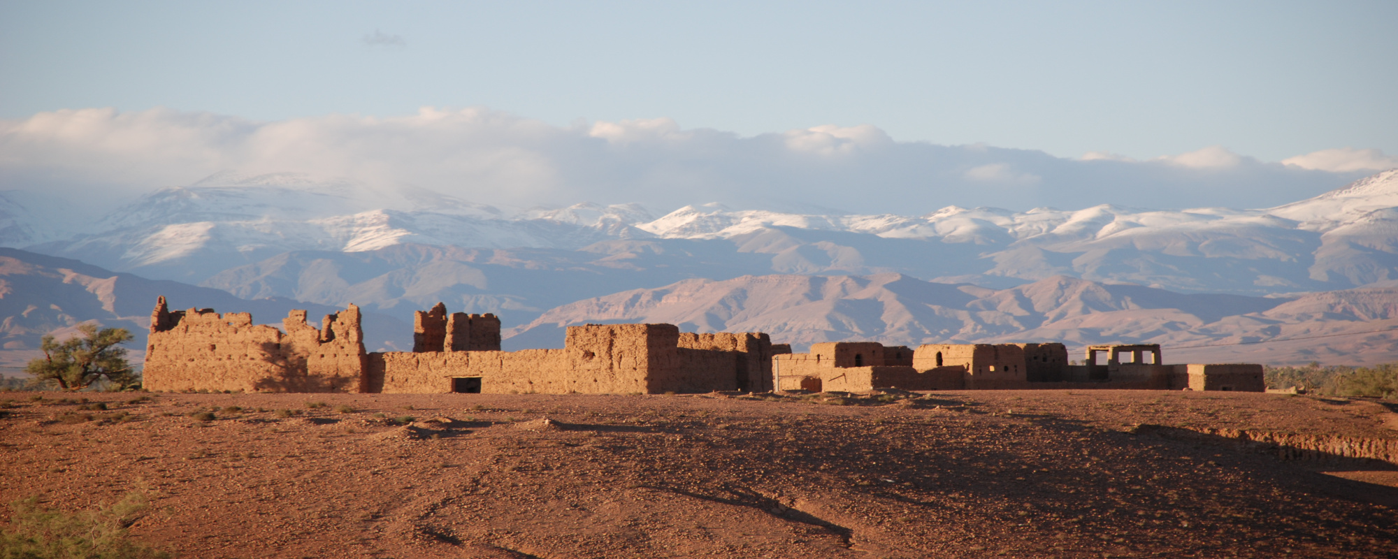 Marokko - Ruinen auf Hügel entlang der Straße der Kasbahs mit Gebirgen im Hintergrund