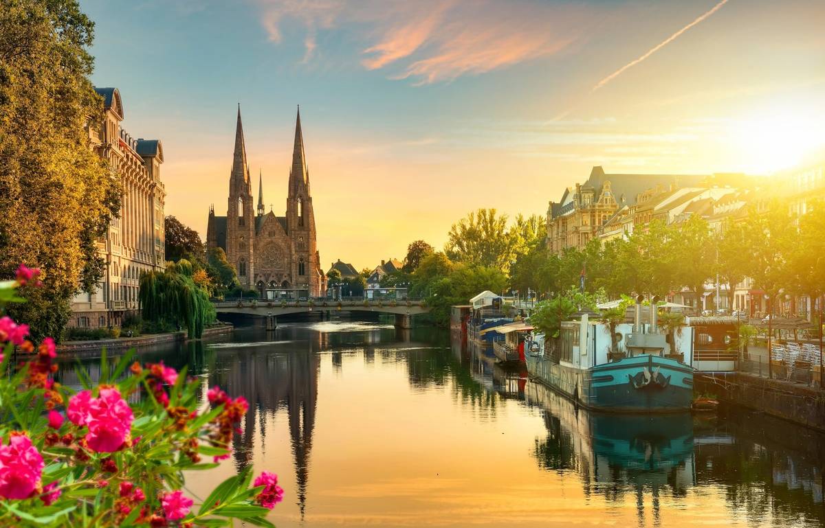 Blick auf Kanal bei Sonnenuntergang mit historischem Gebäude als Blickfang und pinken Blumen im Vordergrund