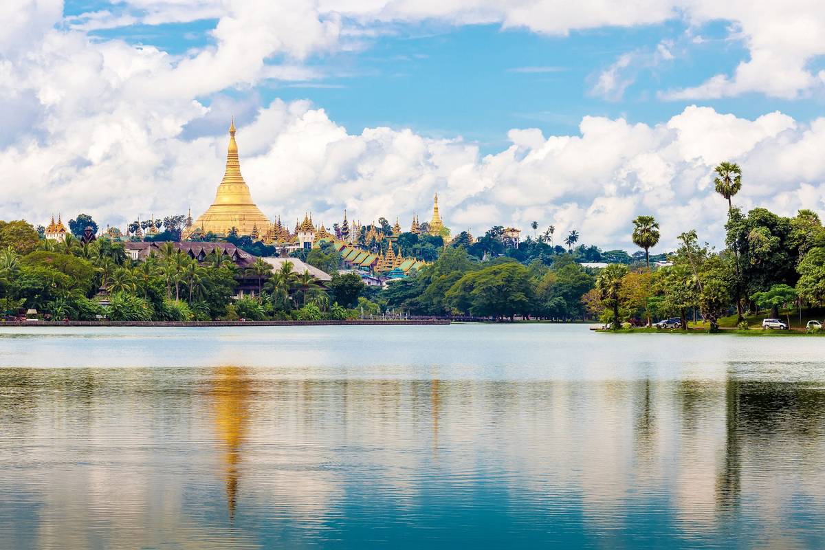 Panoramablick auf die berühmte Pagode in Yangon mit Palmen und Wasser im Vordergrund