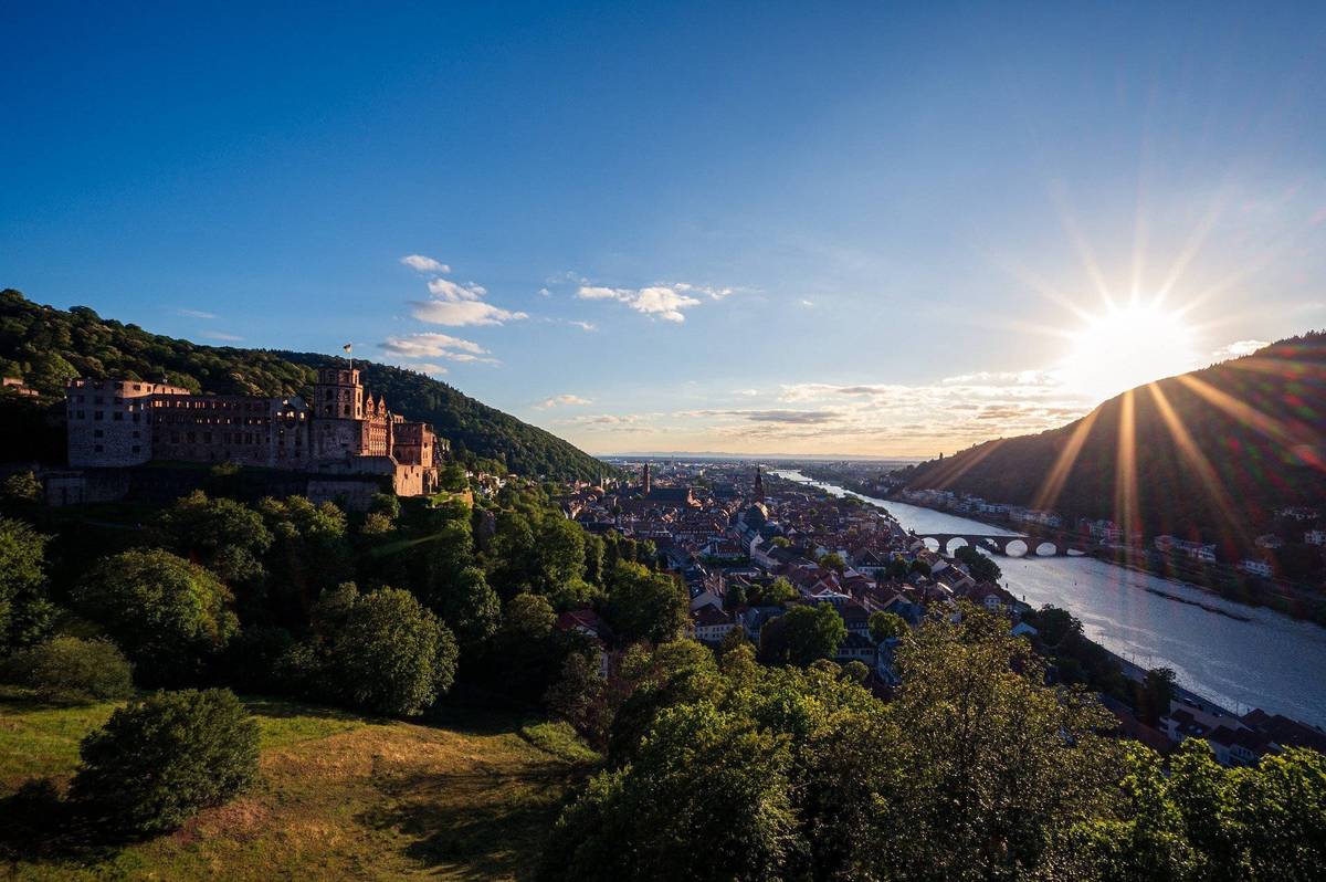 Panoramablick auf Stadt in Hügellandschaft mit Sonnenaufgang und Burg unter blauem Himmel