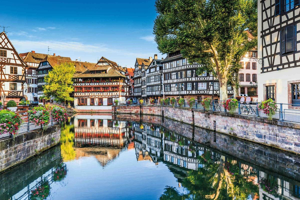 Blick auf historische Fachwerkhäuser am Wasser mit Spiegelung unter blauem Himmel