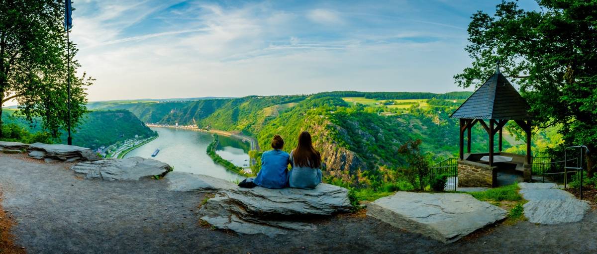 Panoramablick auf Fluss mit grüner Landschaft und zwei Menschen von hinten
