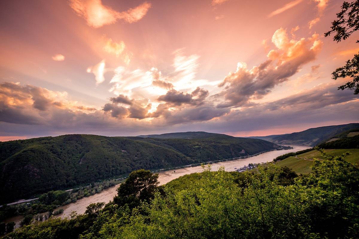 Ausblick auf Fluss mit grünen Hügeln und Bäumen bei Sonnenuntergang