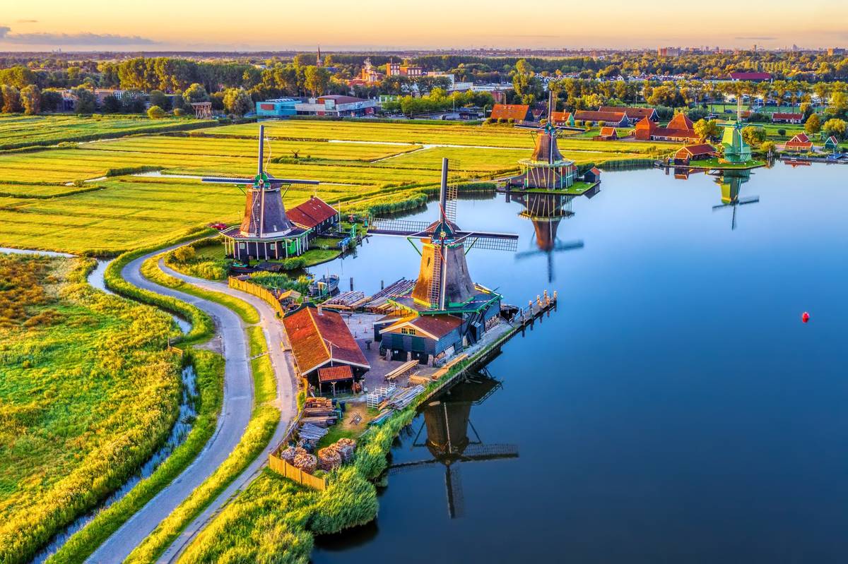 Skyview auf Windmühlen am Wasser mit Grünfläche. Am Horizont ist eine Stadt zu sehen