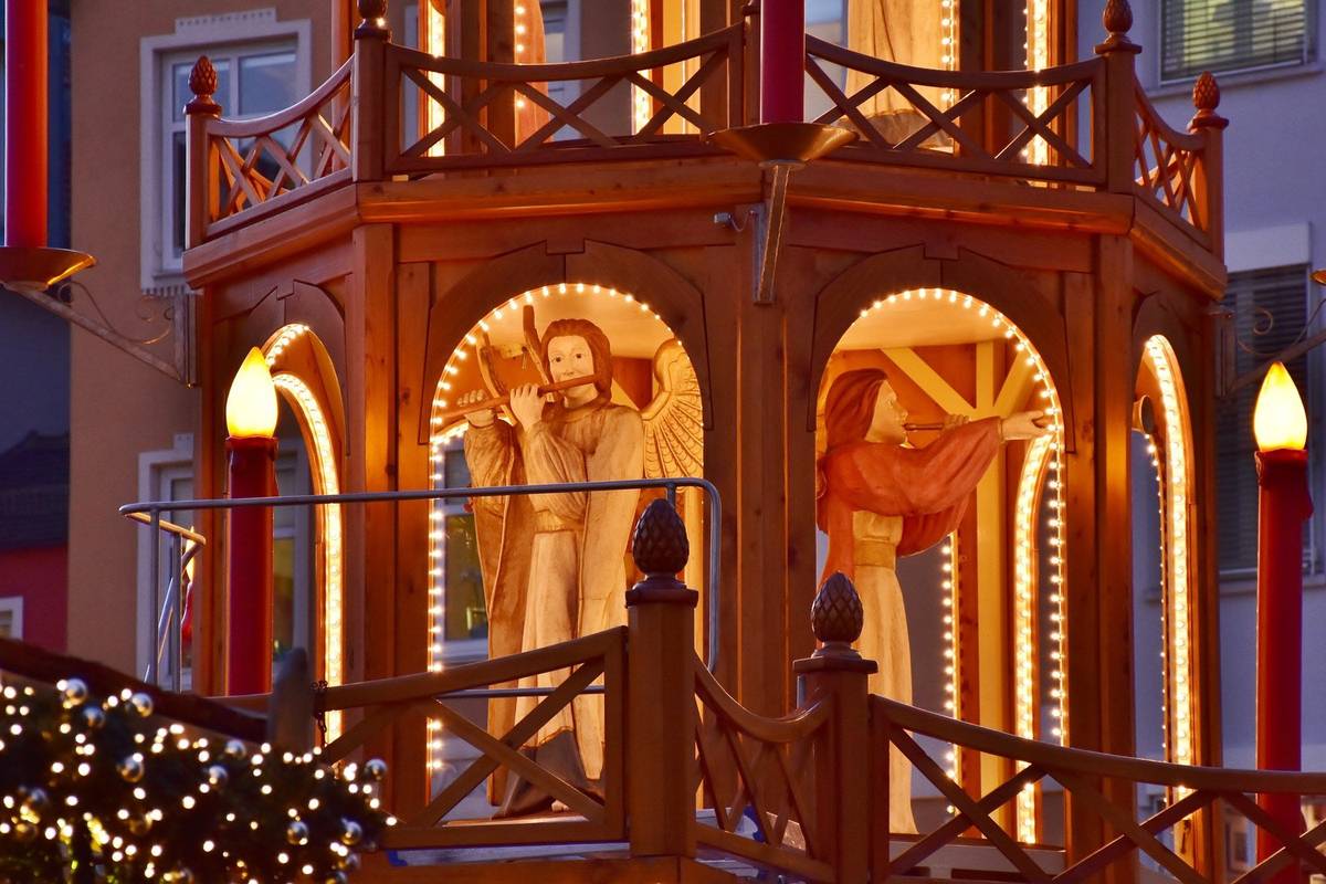 Weihnachtliches Lichtgebilde mit Engelstatuen zwischen Holzbögen