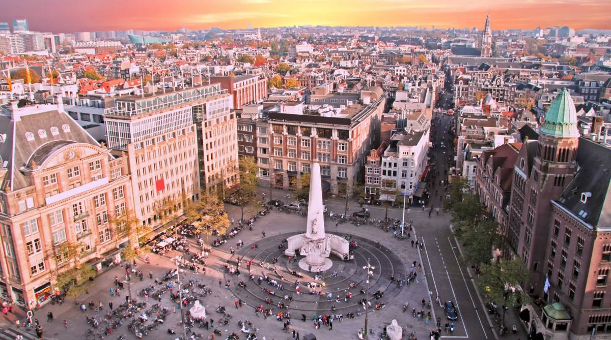 Der Damplatz in Amsterdam in den Niederlanden von oben bei szenischem Sonnenuntergang und mit dem Nationaldenkmal