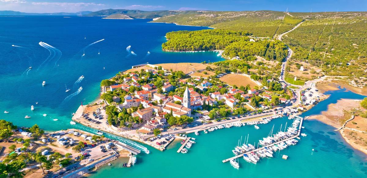 Die Stadt Osor zwischen den Inseln Cres und Mali Losinj von oben zwischen blauem Meer und weitläufiger Grünlandschaft