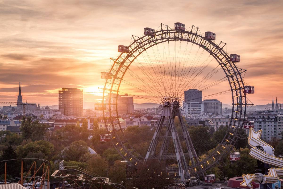 Wiener Riesenrad im Prater bei Sonnenuntergang mit rot beleuchteten Gondeln und stahlgrauem Gestell vor orangegelbem Himmel