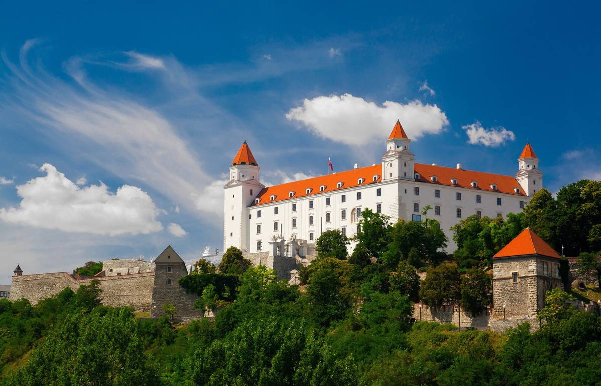Bratislavaer Burg auf Hügel über der Stadt mit weißen Wänden, roten Dächern und grünen Gärten, Blick auf das Schloss bei Tag