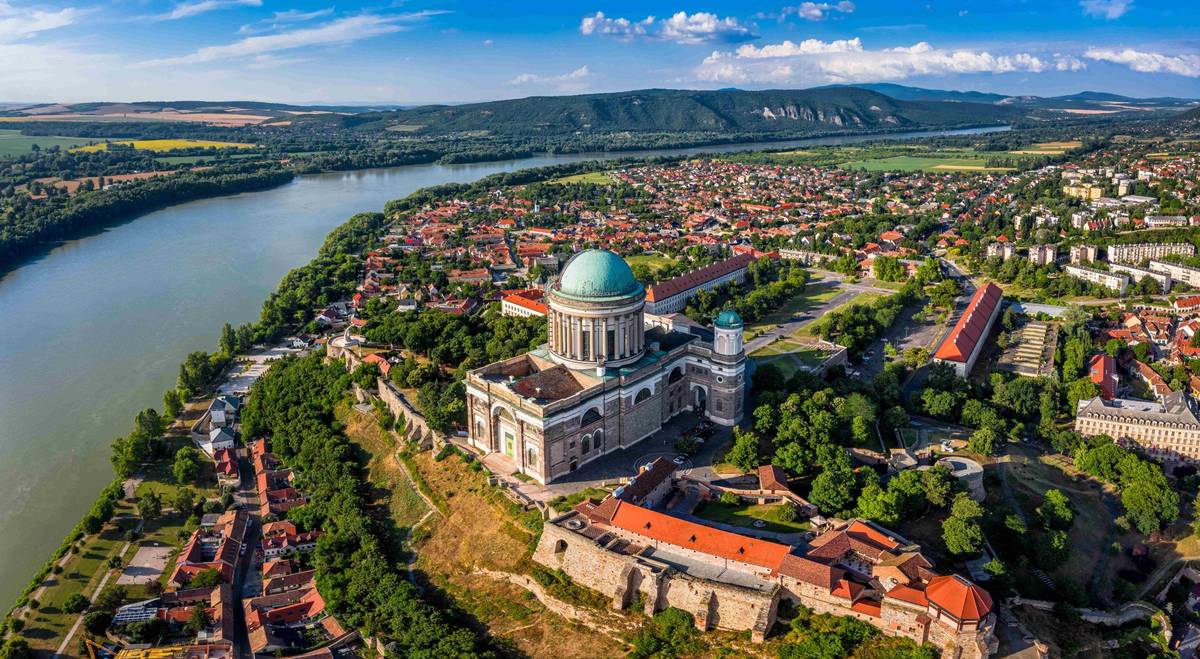 Panoramablick auf die Stadt Esztergom mit der Basilika und dem Donauufer bei Tag, grünen Hügeln und historischen Gebäuden