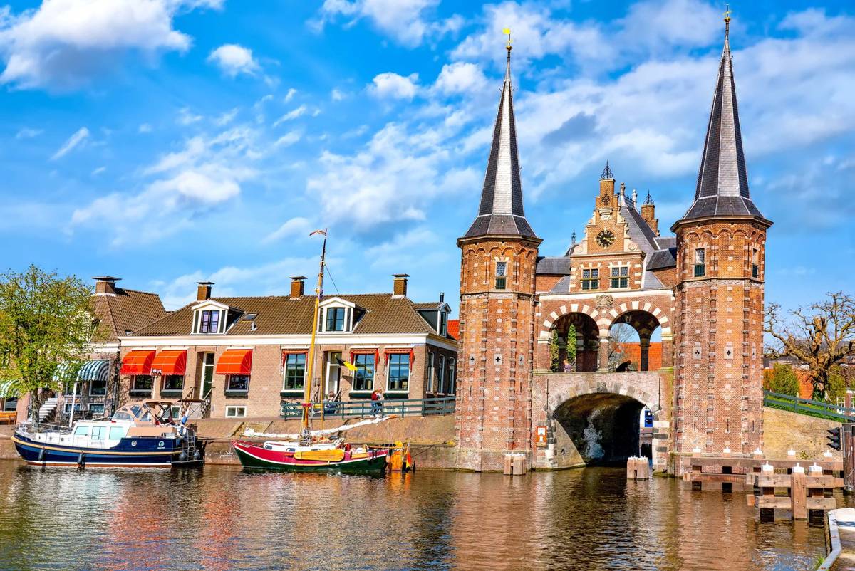 Das Waterpoort in Sneek als frontale Aufnahme. Zwei kleiner Boote liegen neben dem Hafentor an und ein Gebäude mit Markisen ist zu sehen.