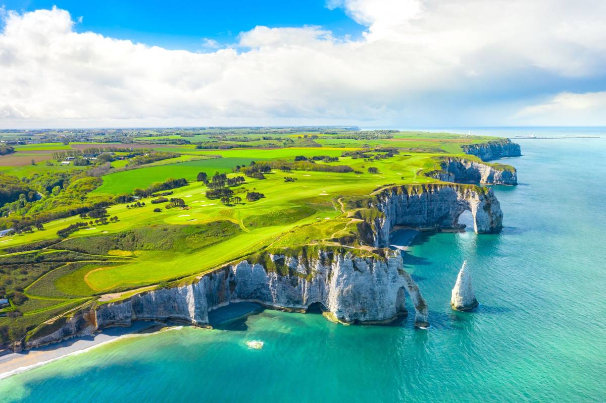 Die steilen Felsklippen von Étretat im Département Seine-Maritime mit türkisem Meerpanorama und grünen Feldern