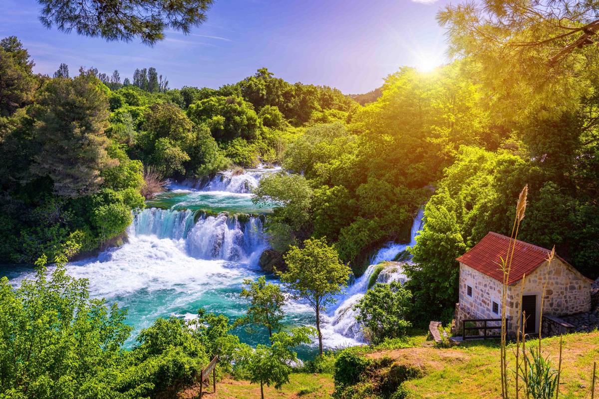 Aufnahme der Krka Wasserfälle mit Sonnenstrahlen zwischen grüner Natur auf dalmatischen Inseln an der Adria