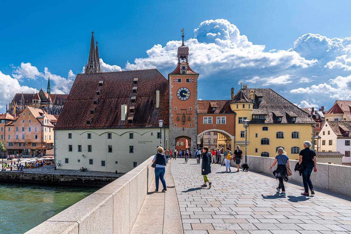 Steinerne Brücke vor dem Stadttor von Regensburg im Sommer bei Sonnenschein und mit vorbeigehenden Passanten