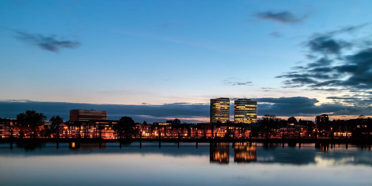 Abendliche Skyline Arnheims mit beleuchteten Fenstern und Spiegelung der Häuser im Wasser des Rheins