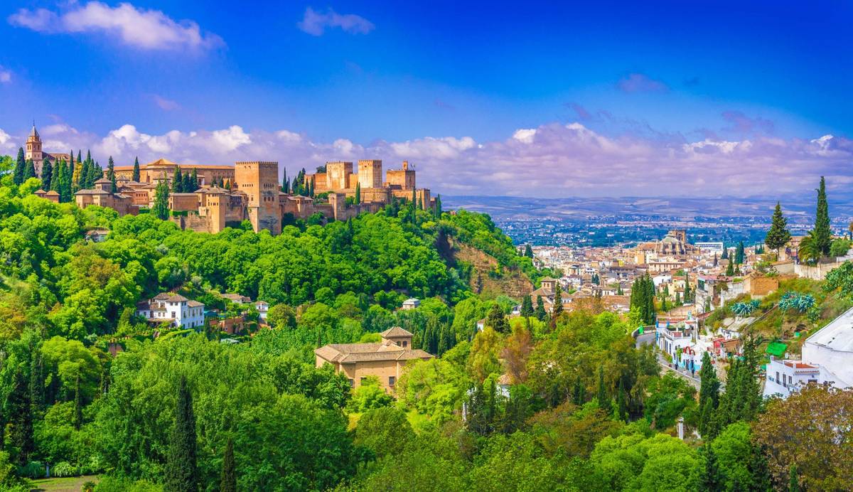 Panoramabild von der Alhambra in Granada im Sommer. Grüne Bäume umgeben die Sehenswürdigkeit und rechts auf dem Bild ist die Stadt zu sehen