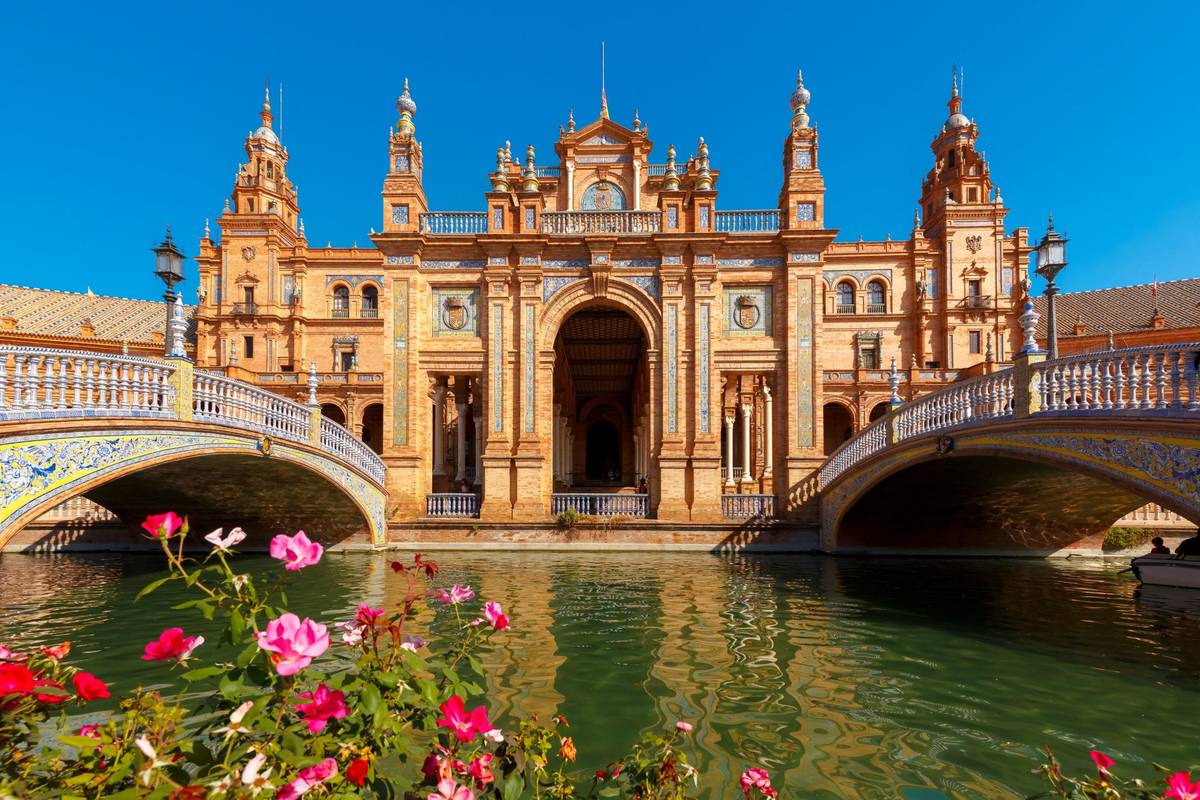 Blick auf historisches Gebäude in Sevilla mit zwei Brücken und Blumen im Vordergrund