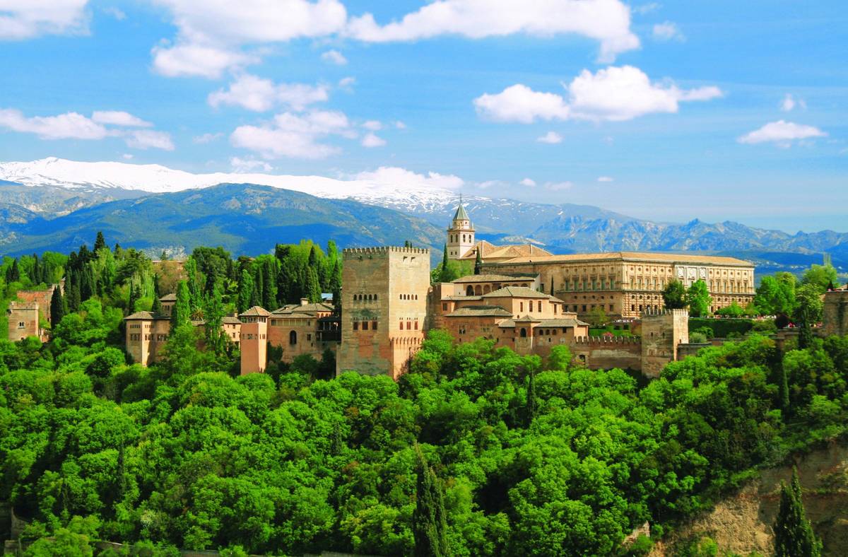 Panoramaaufnahme von der Alhambra in Granada im Sommer bei blauem, leicht bewölktem Himmel. Bergkette im Hintergrund rundet Aufnahme ab