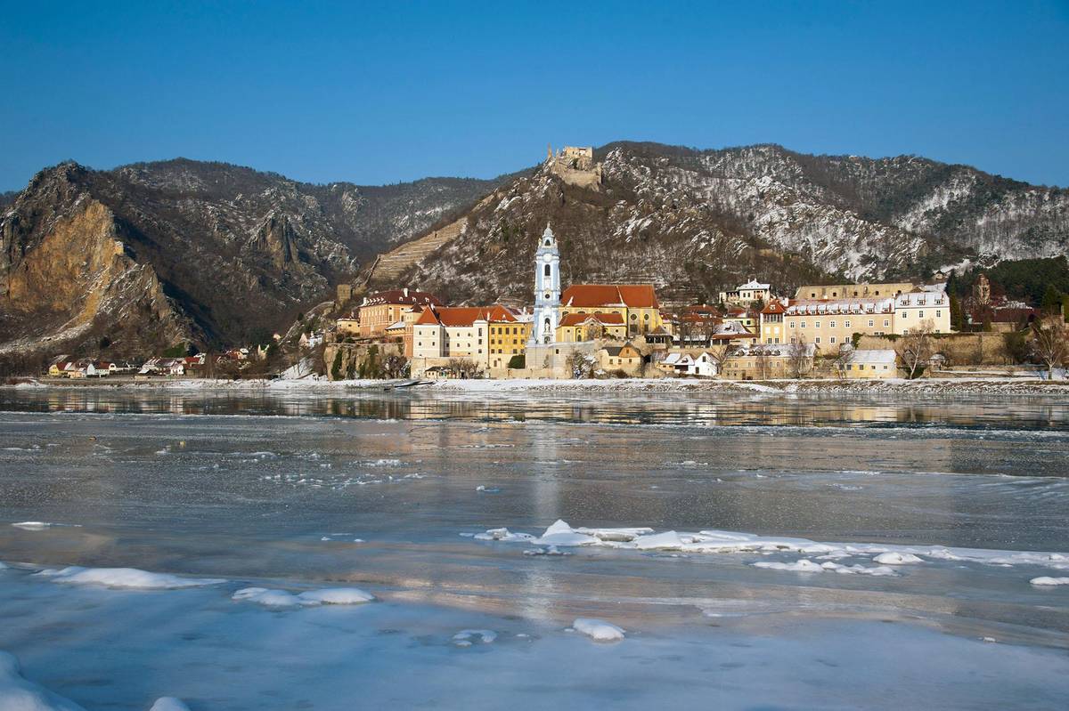 Schneebedeckte Donaulandschaft mit Blick auf die historische Kirche in Dürnstein in der Wachau zur Weihnachts-Flusskreuzfahrt.