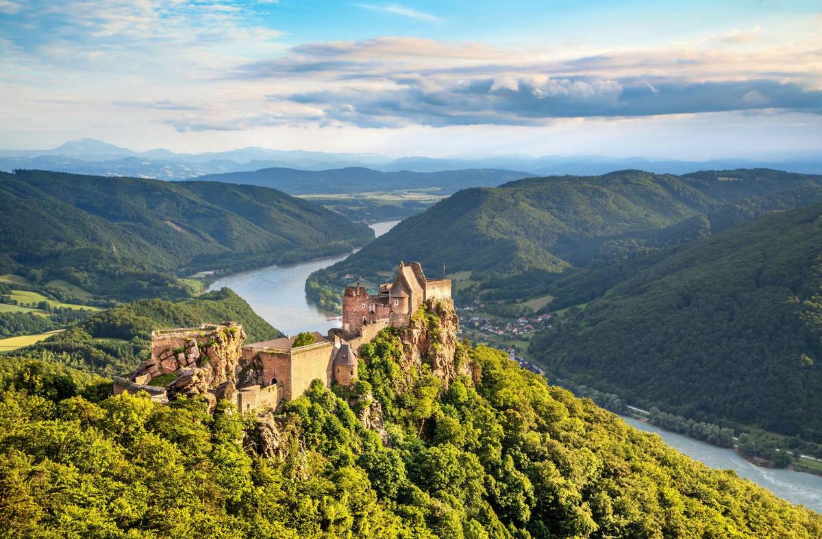 Burgruine auf Hügel, weite Landschaft der Wachau mit Flusswindungen, grünen Hügeln und Weinbergen unter klarem Himmel