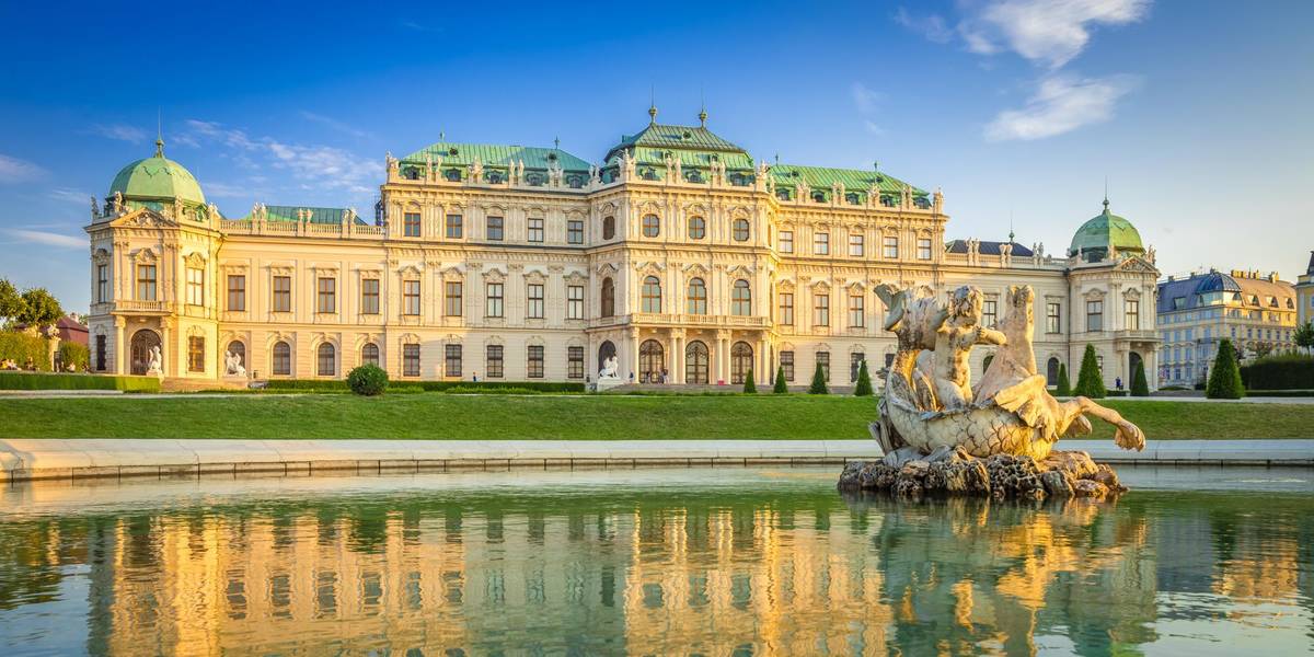 Das Schloss Belvedere in Wien mit seiner Brunnenstatue im Vordergrund wird bei blauem Himmel von der Sonne angestrahlt