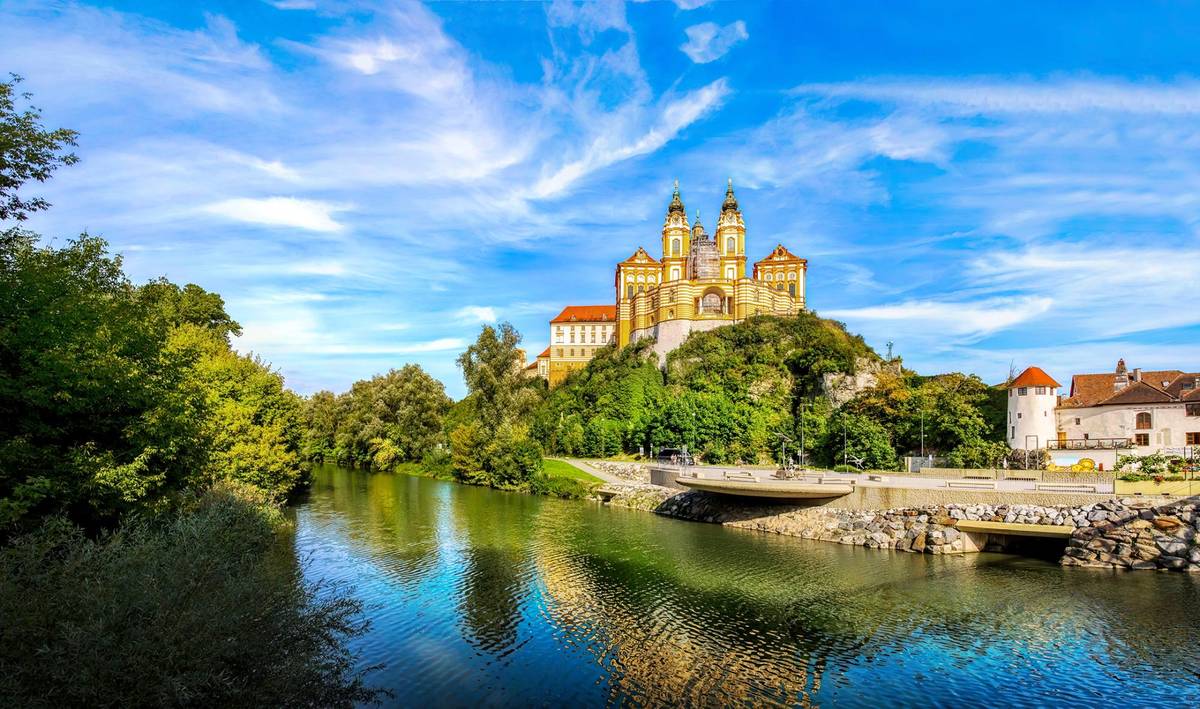 Das berühmte Stift Melk oberhalb eines Donauseitenarms bei strahlen blauem Himmel und Sonnenschein.