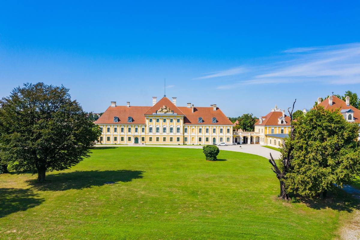 Das barocke Schloss Eltz bei strahlend blauem Himmel in Vukovar. Vor dem Schloss sieht man einen Teil des Schlossgartens mit saftig grünen Bäumen