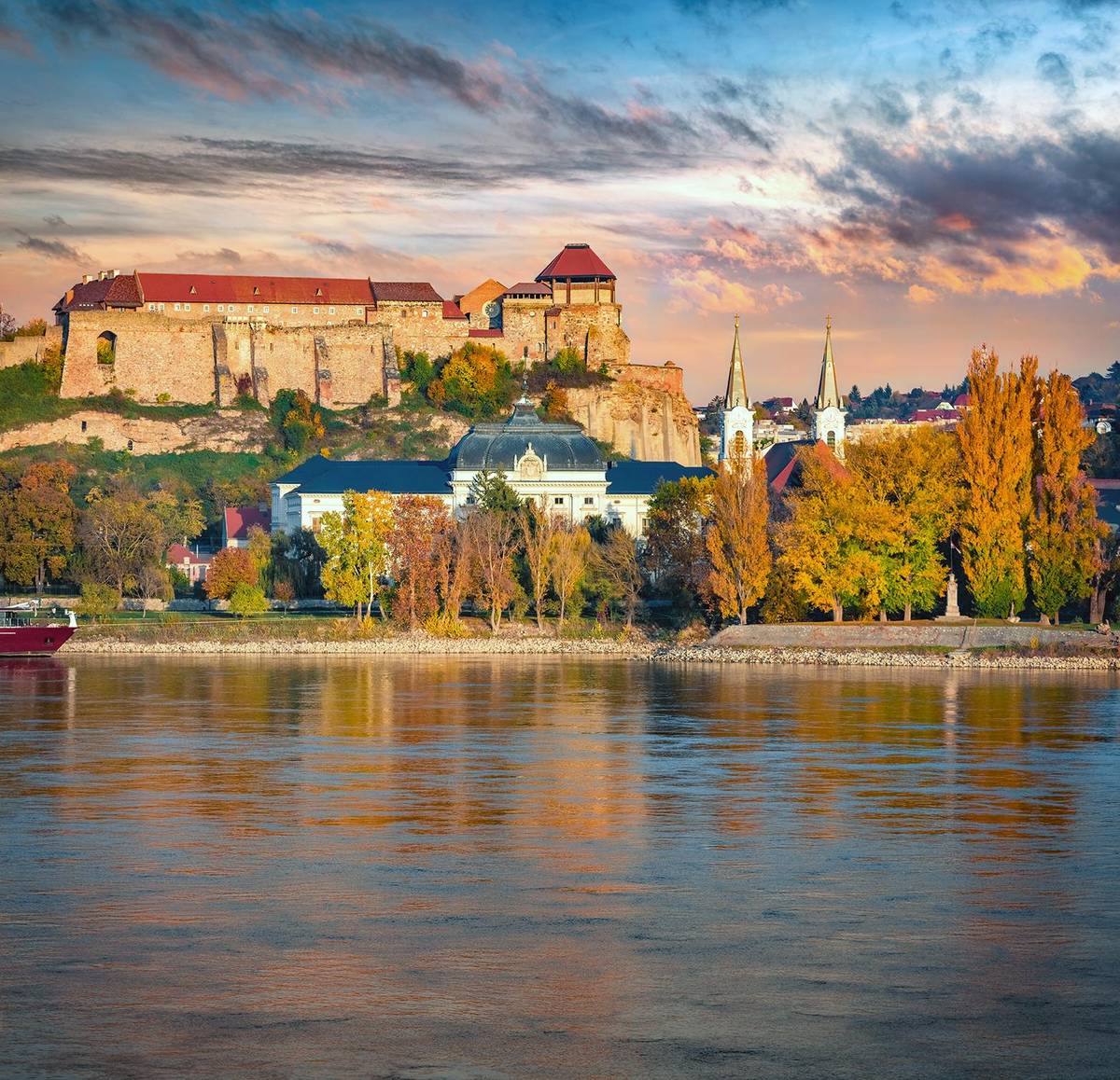 Spätsommerlicher Abend an der Donau und man sieht die kleinere St. Ignatius Kirche am Fuße der Basilika von Esztergom.
