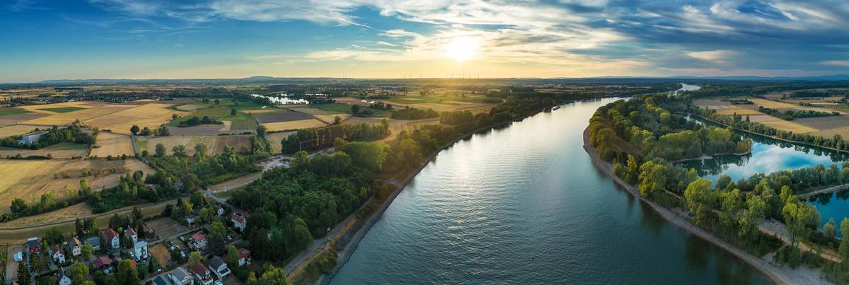 Schöner Ausblick auf die malerische Landschaft am Rhein in sommerlicher Abendstimmung. Die Sonne under der Himmel spiegeln sich über dem Wasser