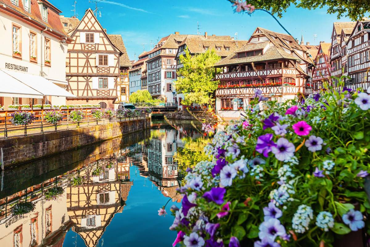 La Petit France bei sommerlichem Wetter und klarem Himmel. Vorne im Bild sind Blumen in dem ehemaligen Gerberviertel von Straßburg zu sehen.