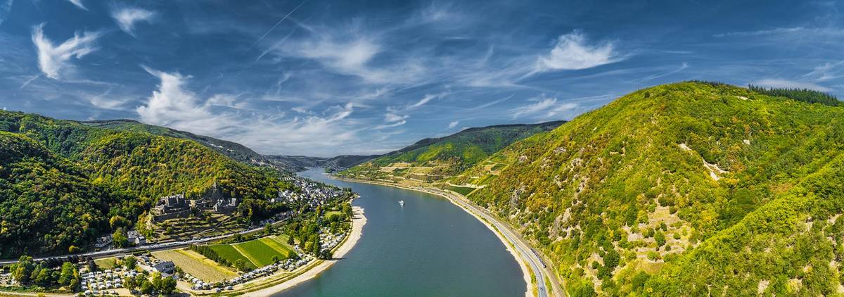 Schöne Aussicht auf die malerische Landschaft des Rhein Tals. Der Himmel ist leicht bewölkt und die Natur am Ufer saftig grün.