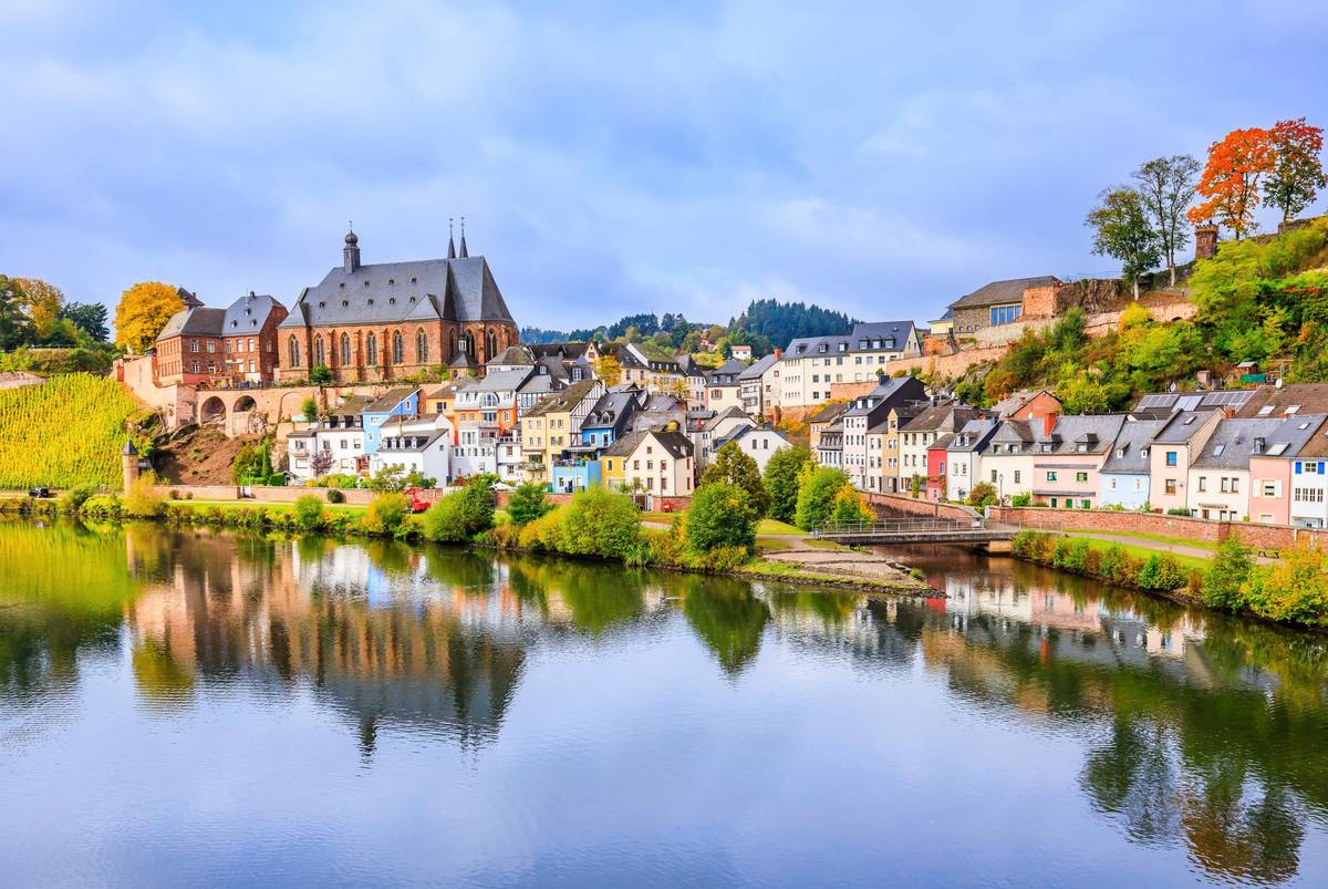 Malerischer Blick auf das beschauliche Städtchen Saarburg. Die Stadt spiegelt sich im Wasser und der Himmel ist klar.